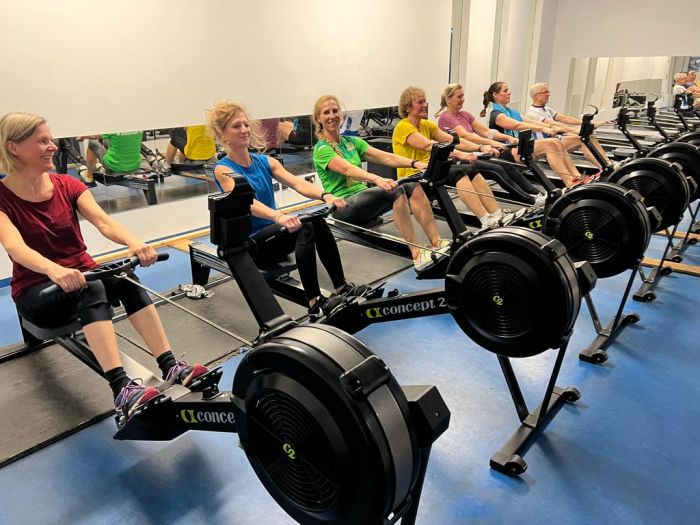 Ruderinnen sitzen nebeneinander auf mehrere Ergometer-Rudergeräten